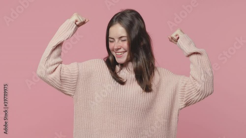Strong cheerful brunette young woman 20s years old in casual pastel sweater posing isolated on pink color background in studio. People lifestyle concept. Looking camera aside showing biceps mucles photo