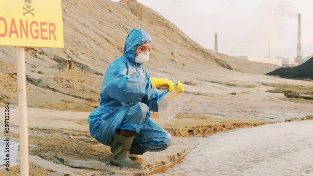Medium shot of female ecologists in protective suits and respiratory masks collecting material evidence from toxic polluted water into test tubes and placing it in individual packs Medium shot of female ecologists in protective suits and respiratory masks collecting material evidence from toxic polluted water into test tubes and placing it in individual packs