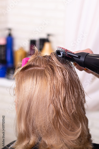 Female hairdresser's hand brushing and blow drying blonde hair in beauty salon