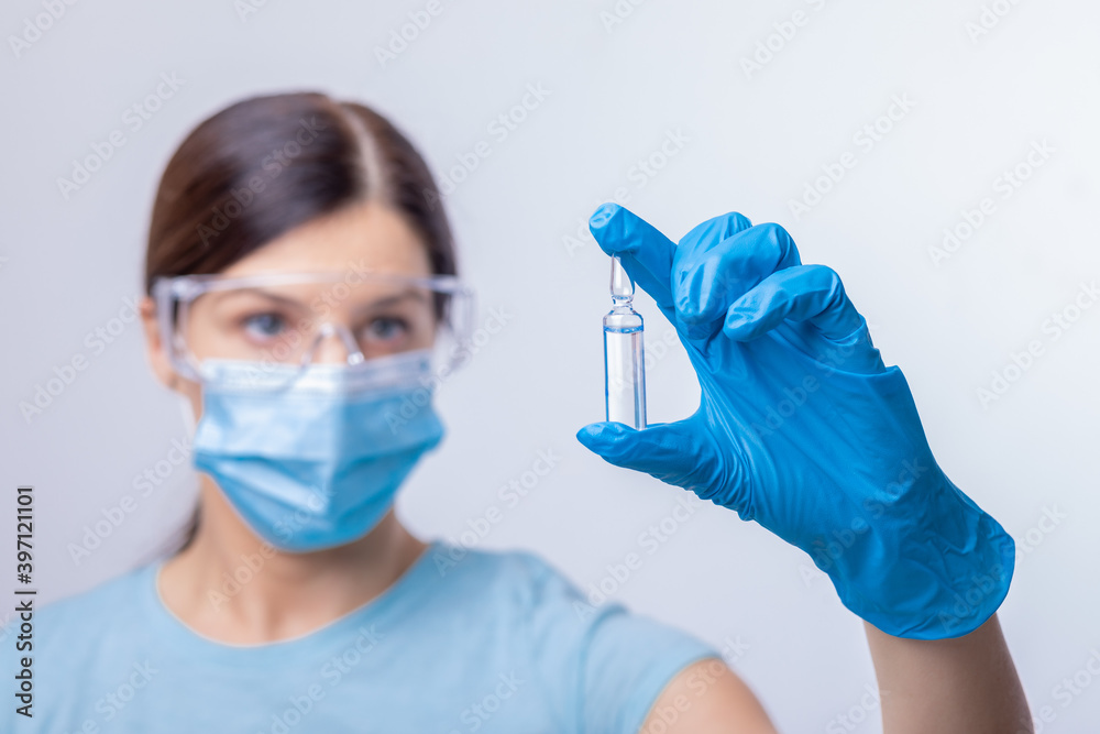 Doctor in protective gloves and mask holding glass vial with injection liquid. Vaccination against influenza and coronavirus.