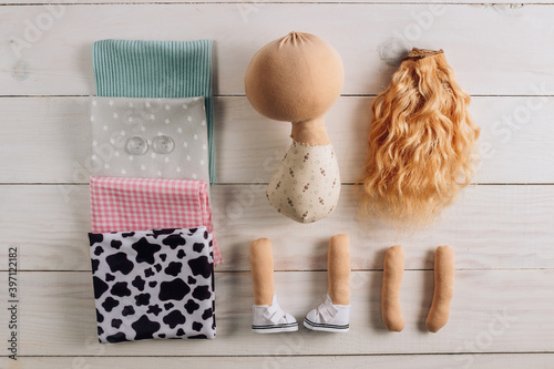 Textile doll in the sewing process with accessories and materials: fabric, thread, shoes on white wooden background. Top view. Flat lay. photo