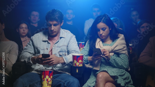 Frustrated woman and man looking mobile phone screen in movie theater.
