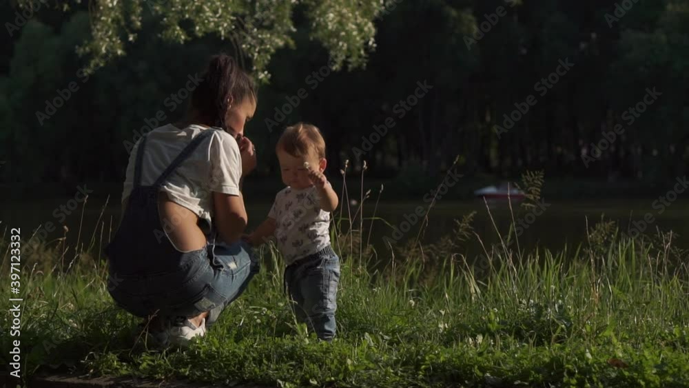Beautiful scene of mother and toddler in park. Mom giving baby son flower and child waving it. Emotional portrait of kid learning about world around, experiencing nature. Concept of single mother. Beautiful scene of mother and toddler in park. Mom giving baby son flower and child waving it. Emotional portrait of kid learning about world around, experiencing nature. Concept of single mother.