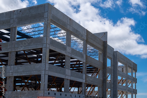 A large multiple storey precast grey concrete building with steel beams against a blue sky. The industrial structure in the corner of a skyscraper building with prefabricated engineering formwork.