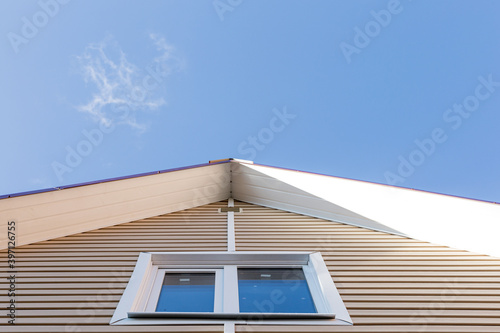 The facade of the new house clad with siding, with windows, against the blue sky.
