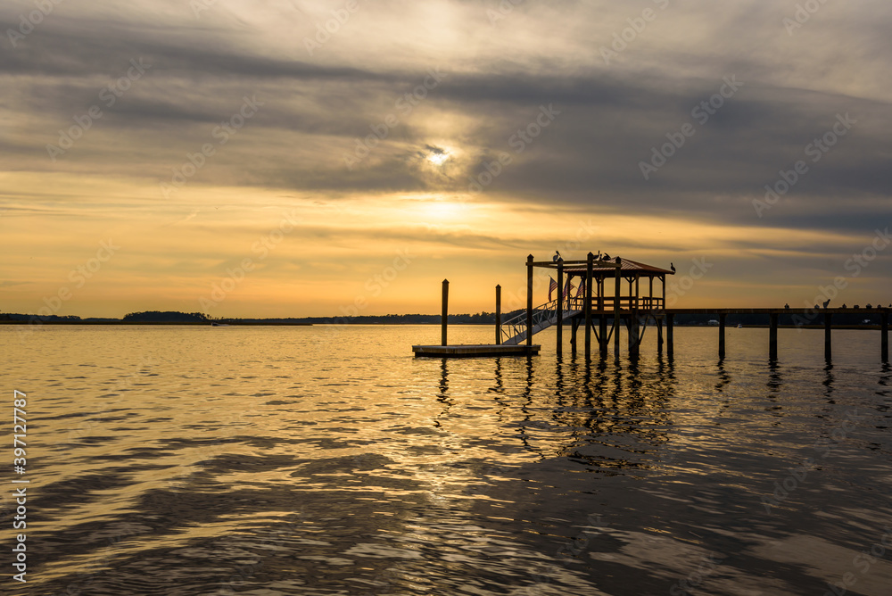 Cloudy Golden Sunset Sunrise on a River with a Dockhouse and Perched Birds in Silhouette Cloudy Golden Sunset Sunrise on a River with a Dockhouse and Perched Birds in Silhouette