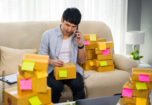 man entrepreneur talking smartphone and prepare parcel boxes for deliver to customer at home office, (SME business)