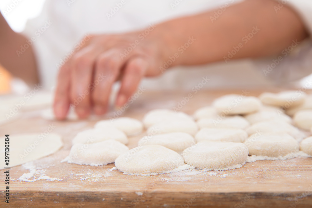 Small dough scattered on the cutting board and hands making dumplings in the background