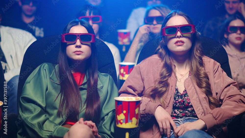 Obraz premium Shocked women watching film in cinema. Scared girl closing face in dark hall.