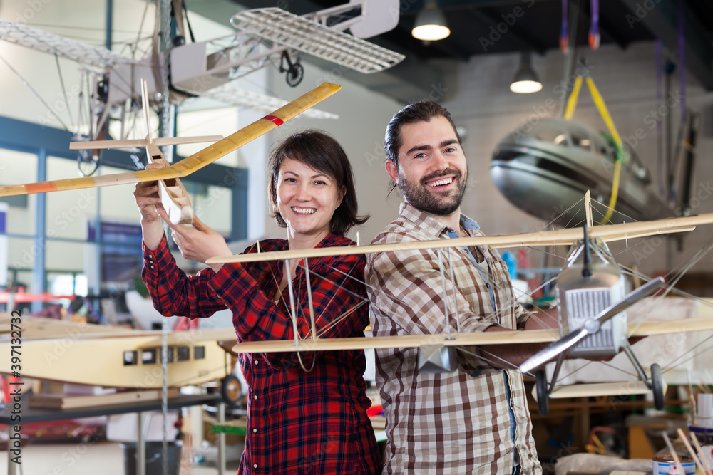 Portrait of attentive female and male hobbyists with plane models created by them in aircraft workshop