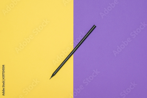 Thin black pencil on a yellow and purple background.