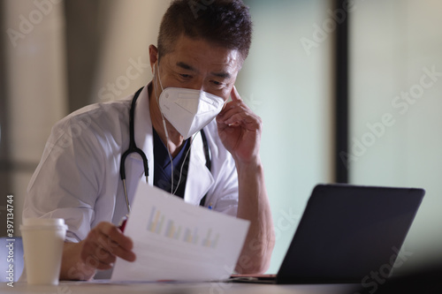 ノートパソコンとマスクをつけたシニア世代の日本人医師