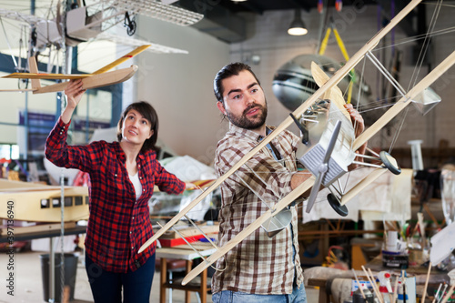 Portrait of cheerful couple having fun with light plane models in aircraft hangar