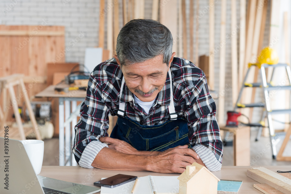 Senior asian elderly old man carpenter using laptop to study and search building idea for build diy furniture in workshop Senior asian elderly old man carpenter using laptop to study and search building idea for build diy furniture in workshop