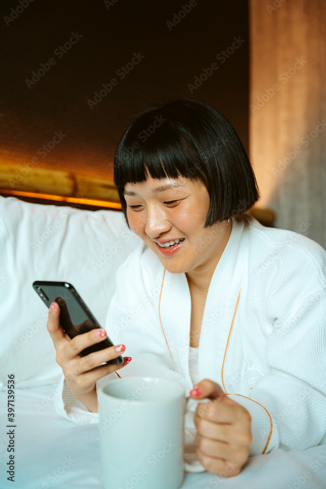 Short hair woman using smartphone on bed and holding coffee cup. Short hair woman using smartphone on bed and holding coffee cup.