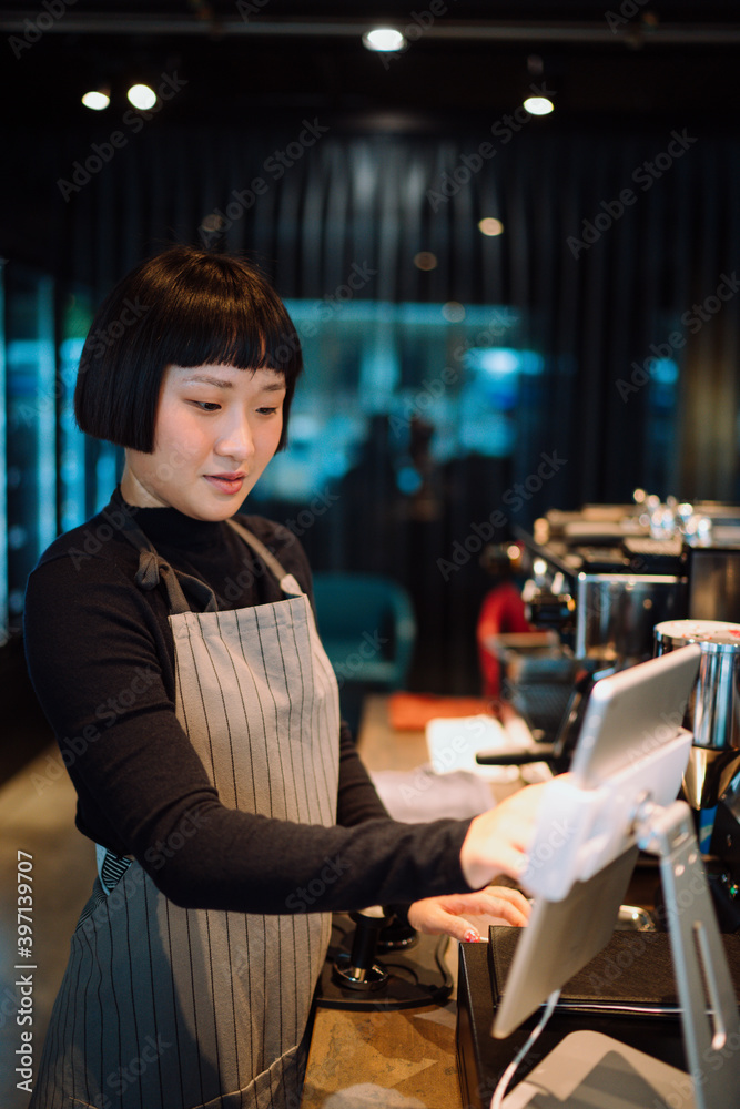 Barista woman using digital tablet for paying bill in cafe.