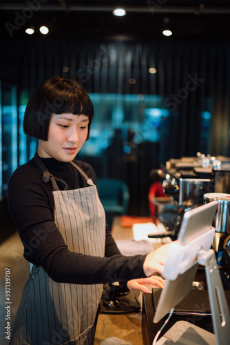 Barista woman using digital tablet for paying bill in cafe.
