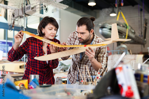 Happy cheerful smiling couple enjoying their hobbies - modeling light airplanes in aircraft hangar