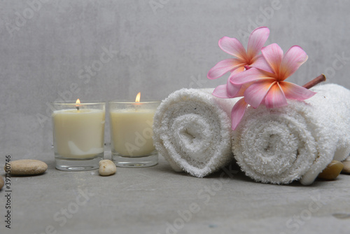 Spa setting with plumeria flowers, candles and gray stones and rolled towel on gray background 