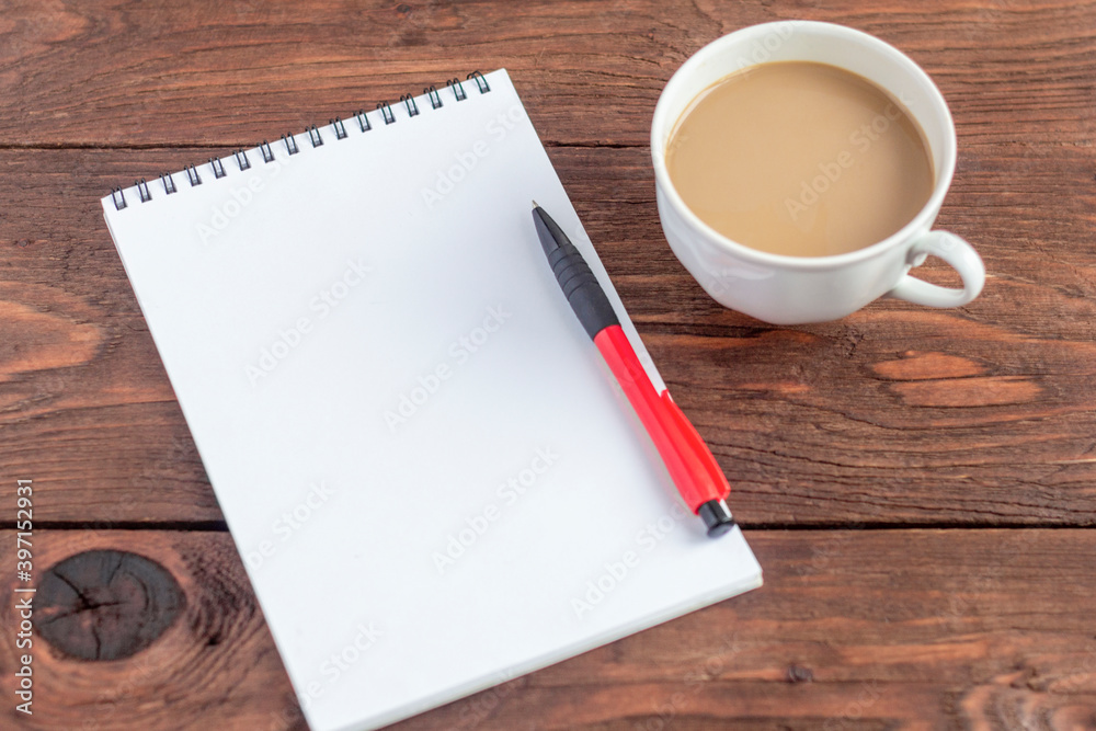 A Cup of coffee with milk and a Notepad with a pen on an old wooden table. A Cup of coffee with milk and a Notepad with a pen on an old wooden table.