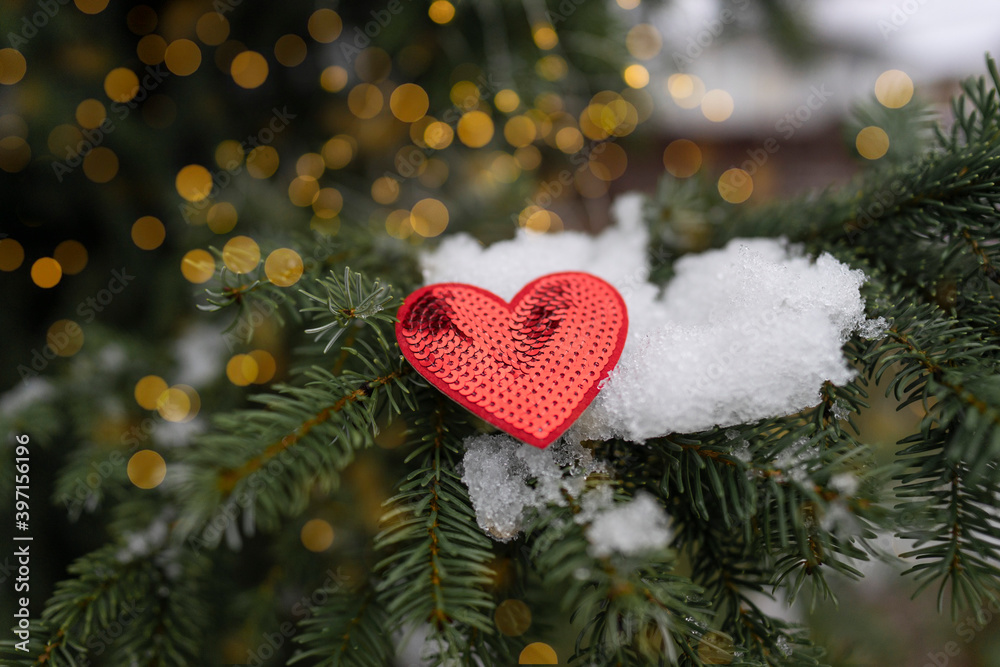 A red heart as a symbol of Valentine's Day lies on the tree with bokeh lights at the background