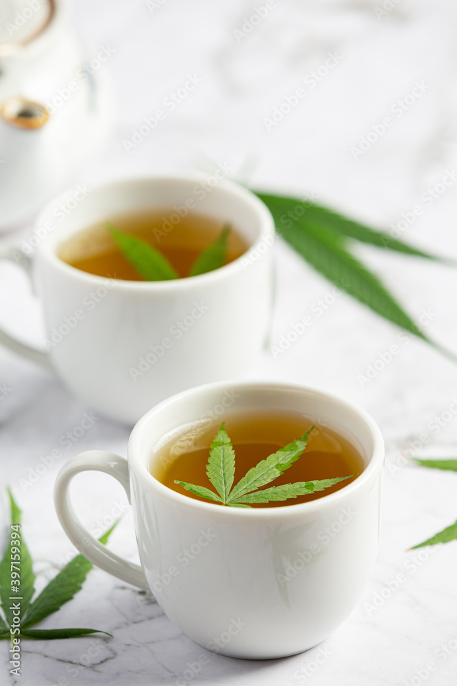 two cups of hemp tea with hemp leaves put on white marble floor two cups of hemp tea with hemp leaves put on white marble floor