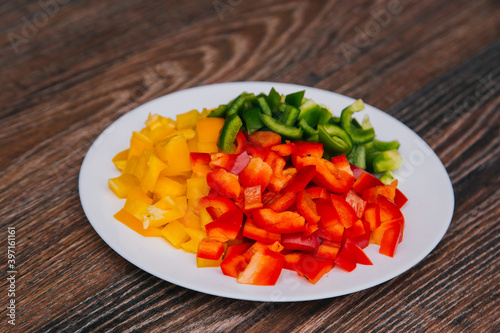 Diced multi-colored bell peppers on a white plate. On a dark wooden background. Red, yellow and green