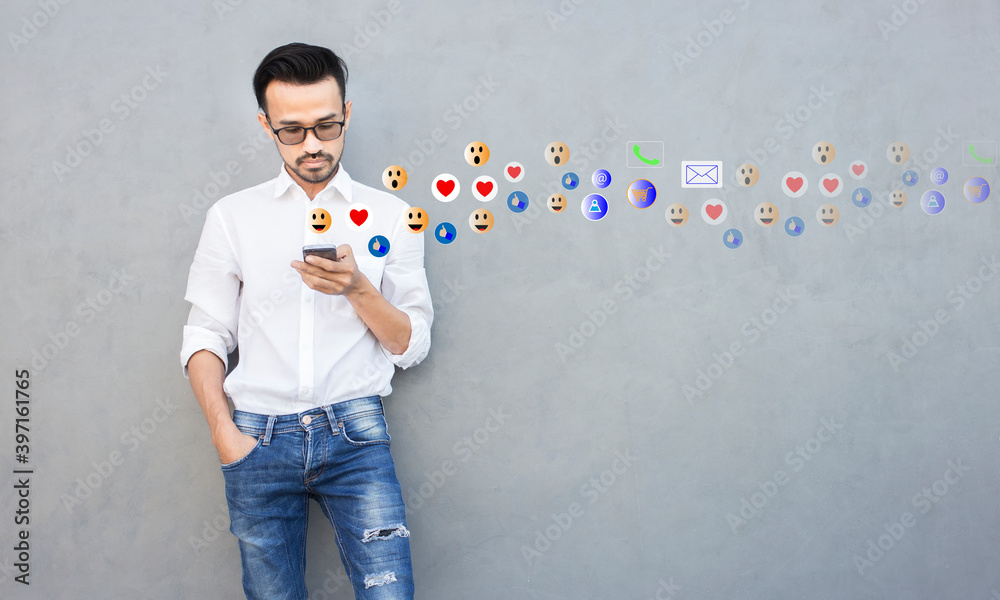 Young man standing and using smartphone with social media network with gray wall copy space, connection, communication and work from home concept Young man standing and using smartphone with social media network with gray wall copy space, connection, communication and work from home concept