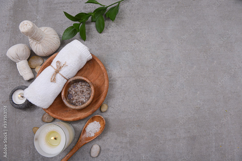 Rolled towels and salt in bowl in wooden bowl, bamboo leaves,stone and,candle on grey background, Copy space for your text Rolled towels and salt in bowl in wooden bowl, bamboo leaves,stone and,candle on grey background, Copy space for your text