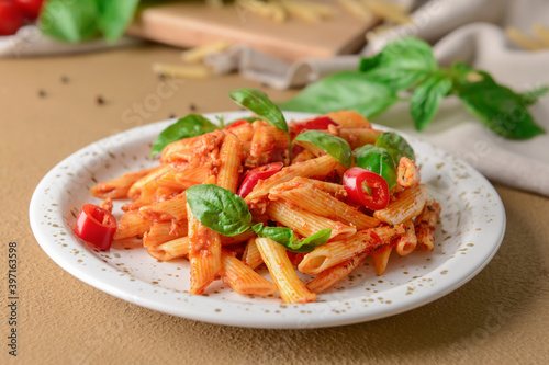 Plate of delicious penne pasta with tomato sauce on table