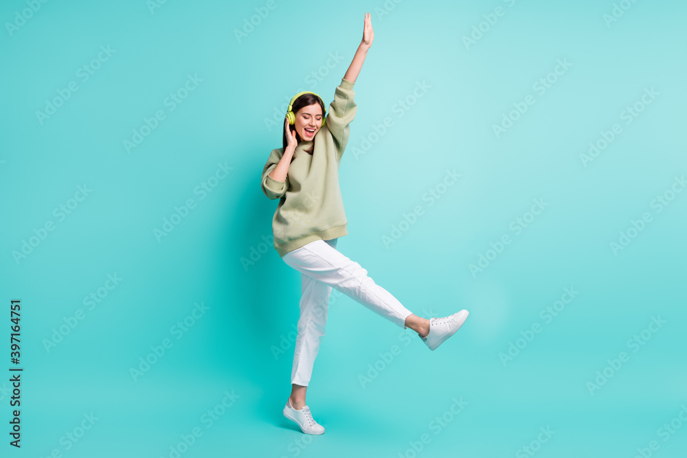 Full length photo portrait of cool woman wearing green headphones dancing standing on one leg isolated on vivid turquoise colored background