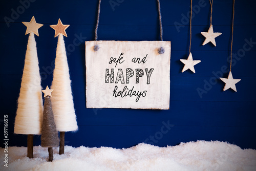 Wooden Sign With Engllish Text Safe And Happy Christmas. White Christmas Tree With Stars. Snow And Blue Background photo