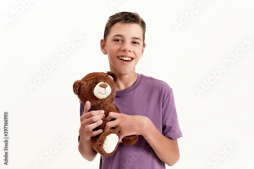 Portrait of happy teenaged disabled boy with cerebral palsy smiling at camera and holding his teddy bear toy, posing isolated over white background photo