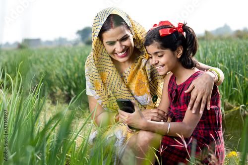 Rural mother and daughter using mobile phone on agriculture field