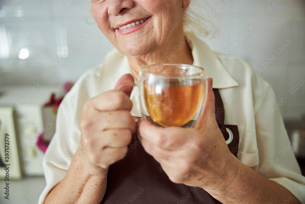 Joyful old woman holding glass cup of tea Joyful old woman holding glass cup of tea
