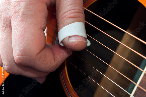 Detail of a guitar player hand using a thumbpick to play fingerstyle and fingerpick music photo