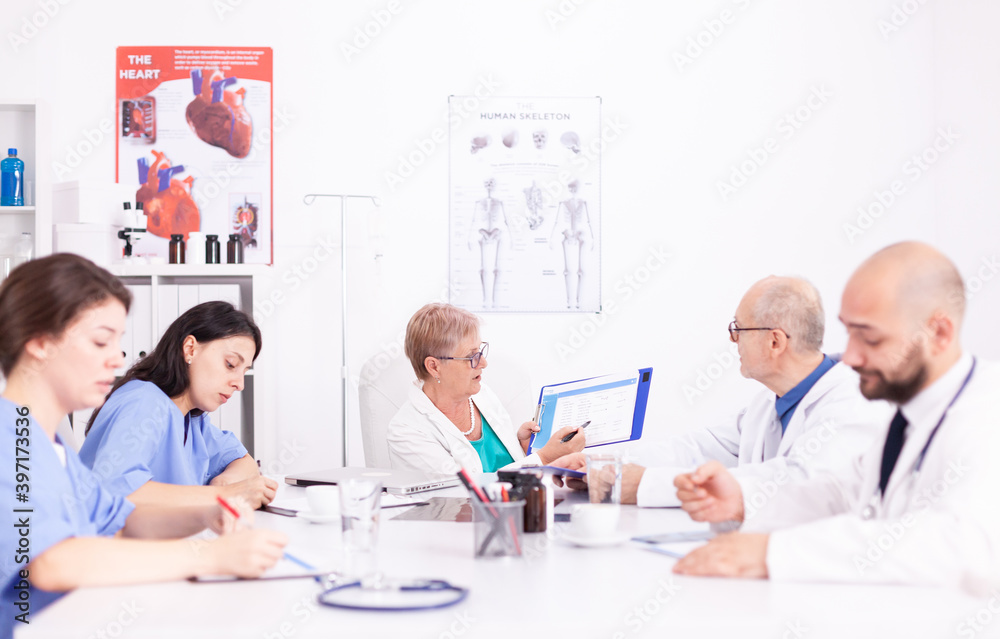 Obraz premium Female nurses taking notes while medical expert explaining about viral diseases in hospital conference room. Clinic expert therapist talking with colleagues about disease, medicine professional