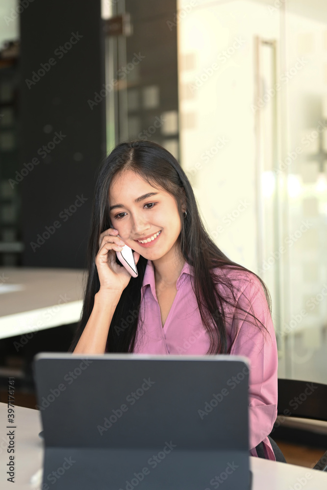 Portrait of a young businesswoman is talking on mobile phone while working with computer tablet in office. Portrait of a young businesswoman is talking on mobile phone while working with computer tablet in office.