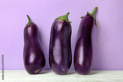 Fresh raw eggplants on white wooden table against violet background
