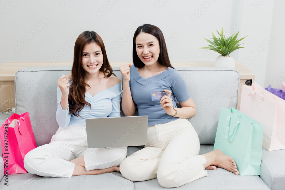 Two Asian beauty people are using a credit card to make purchases using a laptop via the internet. With a happy smiling face, being a new normal online business In the shopping experience from home Two Asian beauty people are using a credit card to make purchases using a laptop via the internet. With a happy smiling face, being a new normal online business In the shopping experience from home