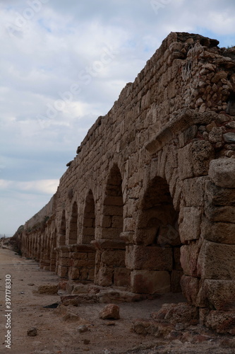 The aqueduct at the Caesarea Equator, Israel. Longitudes create a deep perspective, the stones align in the order of assembly with the background combining a ruptured sky and Mediterranean water.