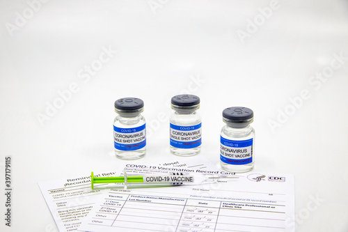 Syringe with COVID-19 vaccine on vaccination record card approved by CDC with corona virus vaccine vials in the background. Concept of vaccination on white background with copy space.