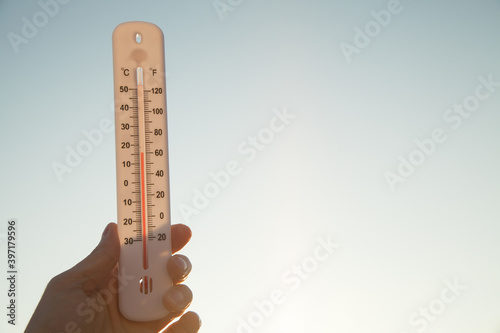 Hand holding thermometer on sky background. photo