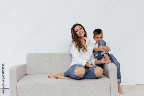 Mom and young son sit at home on a white sofa