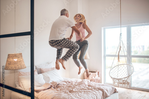 Fotografija Mature couple jumping on the bed and feeling awesome