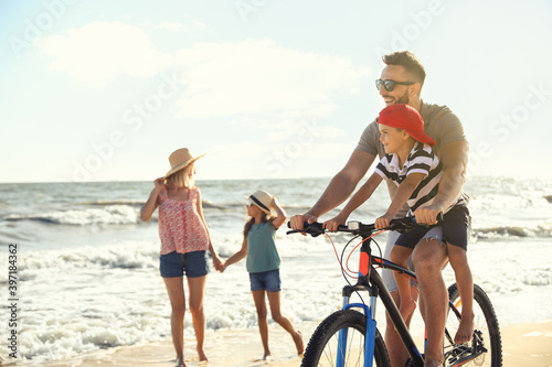 Happy family with bicycle on sandy beach near sea