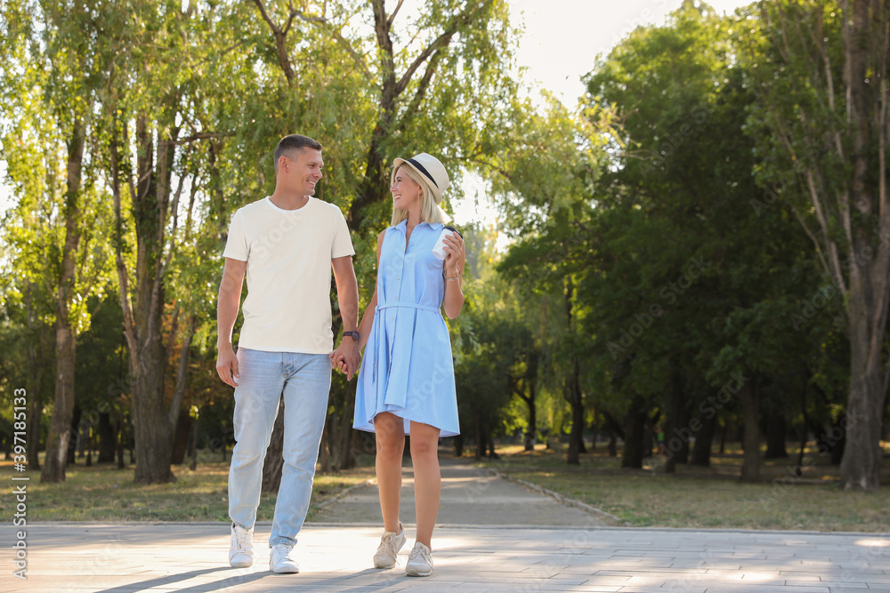 Happy couple with drink walking along park on summer day Happy couple with drink walking along park on summer day