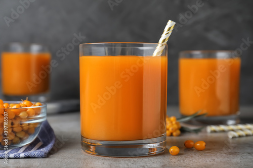 Delicious sea buckthorn juice with straw on grey table, closeup