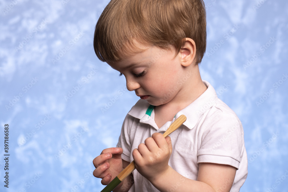 a small child with interest examines a bamboo toothbrush in the bathroom on a blue texture background. horizontal photo. ecologically pure. morning hygiene concept. close-up a small child with interest examines a bamboo toothbrush in the bathroom on a blue texture background. horizontal photo. ecologically pure. morning hygiene concept. close-up