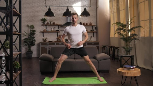 Smiling sporty male practicing yoga at home during covid-19 infection epidemic. Athleltic young man exercising warrior position on yoga mat, home workout, meditation, healthy positive lifestyle photo